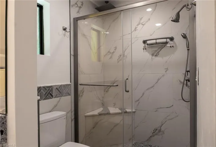 Bathroom featuring tile walls, toilet, a marble finish shower, and a wainscoted wall