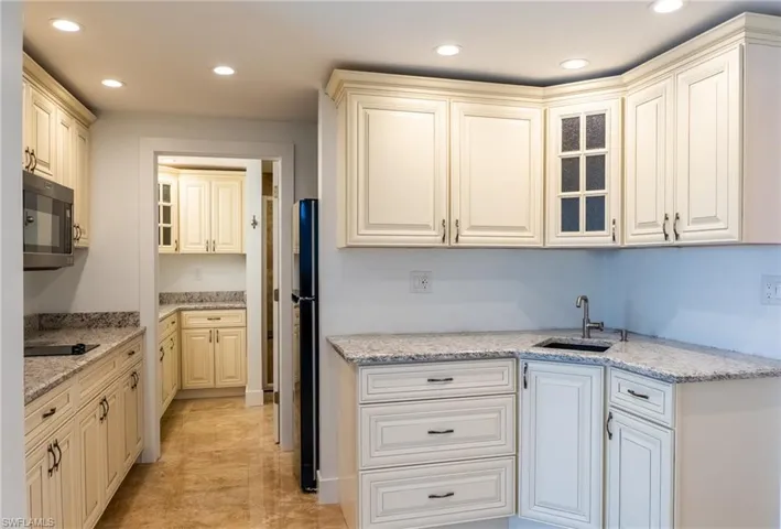 Kitchen featuring recessed lighting, glass insert cabinets, light stone countertops, and a sink