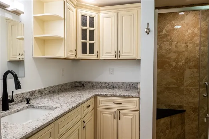 Kitchen with a sink, open shelves, glass insert cabinets, light stone countertops, and cream cabinets
