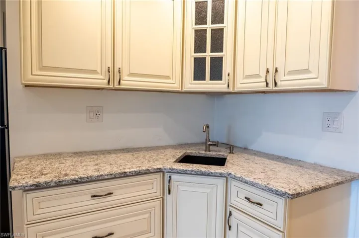 Kitchen featuring glass insert cabinets, cream cabinetry, light stone counters, and a sink