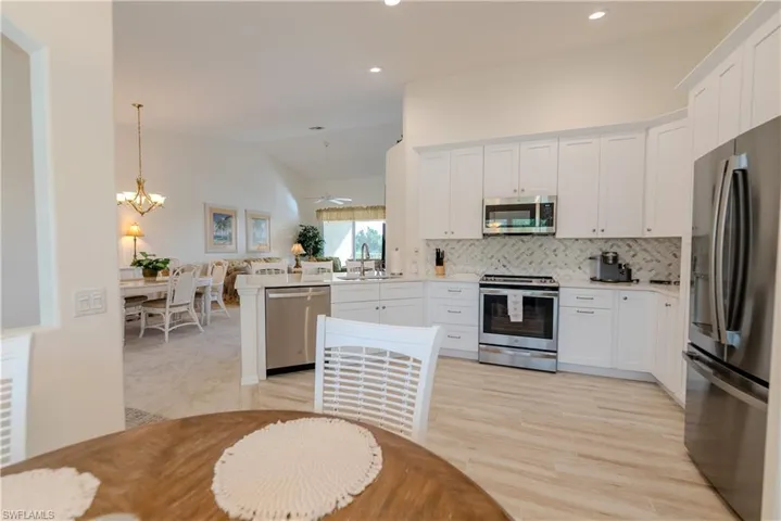Kitchen with a notable chandelier, tasteful backsplash, white cabinets, appliances with stainless steel finishes, and light carpet