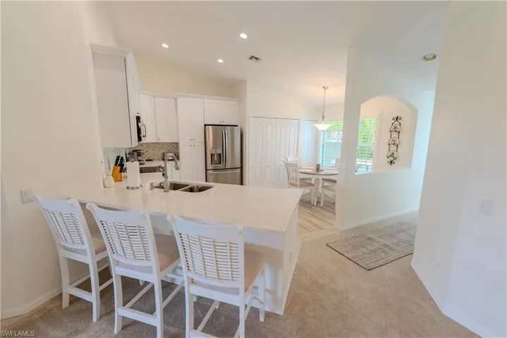 Kitchen with stainless steel fridge with ice dispenser, lofted ceiling, white cabinets, light carpet, and sink
