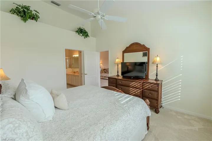 Bedroom featuring light carpet, connected bathroom, ceiling fan, and high vaulted ceiling