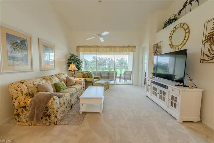 Carpeted living room with high vaulted ceiling and ceiling fan