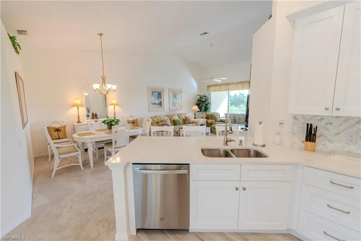 Kitchen featuring white cabinets, ceiling fan with notable chandelier, lofted ceiling, dishwasher, and light carpet