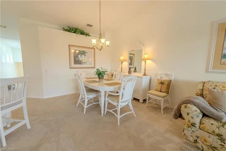 Carpeted dining area with high vaulted ceiling and a notable chandelier