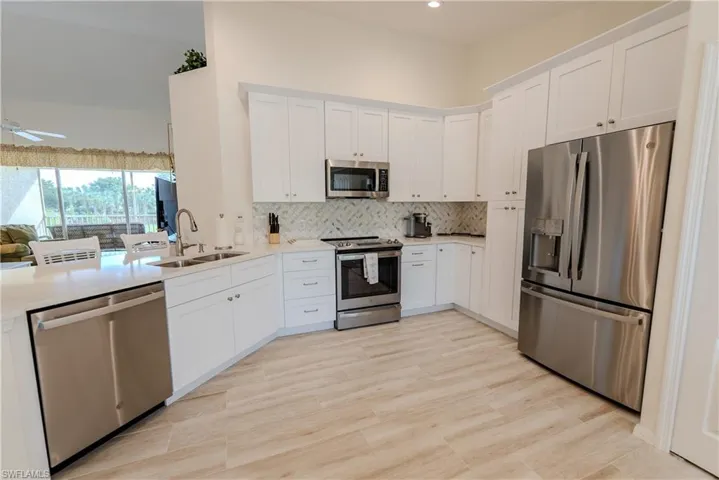 Kitchen with a notable chandelier, tasteful backsplash, white cabinets, appliances with stainless steel finishes, and light carpet