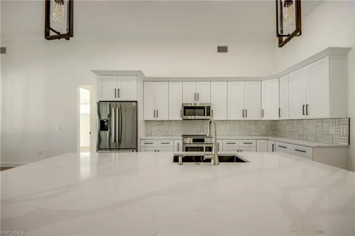 Kitchen with light stone countertops, tasteful backsplash, white cabinets, sink, and appliances with stainless steel finishes