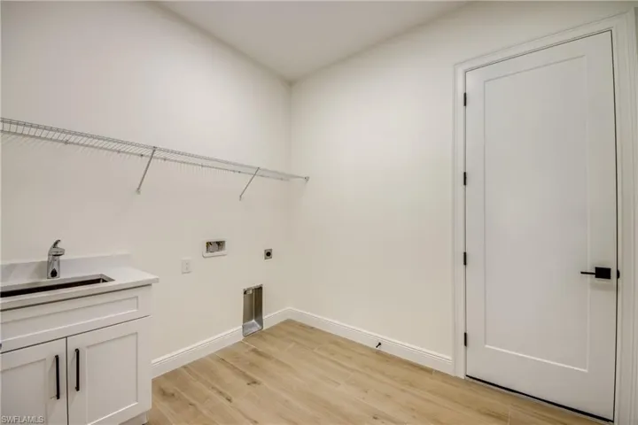 Washroom with light wood-type flooring, hookup for a washing machine, sink, electric dryer hookup, and cabinets