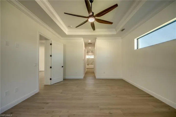 Empty room with ceiling fan, light hardwood / wood-style floors, a raised ceiling, and ornamental molding