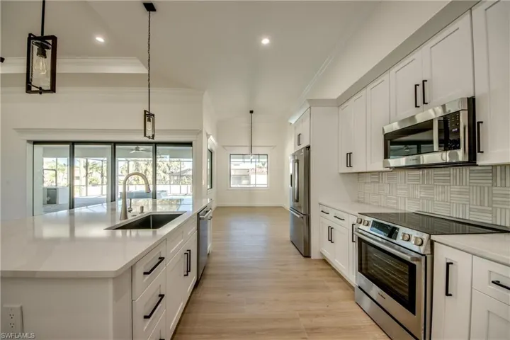 Kitchen featuring a kitchen island with sink, stainless steel appliances, sink, white cabinetry, and decorative light fixtures