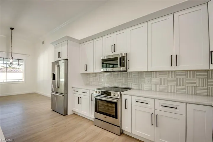 Kitchen featuring light hardwood / wood-style floors, tasteful backsplash, crown molding, white cabinets, and appliances with stainless steel finishes