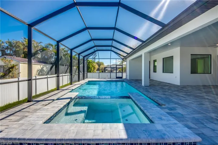 View of pool with an in ground hot tub, glass enclosure, and a patio area