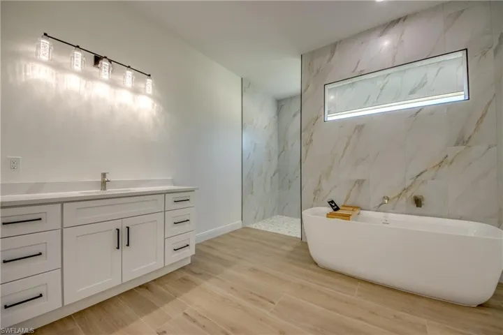 Bathroom featuring wood-type flooring, vanity, tile walls, and shower with separate bathtub
