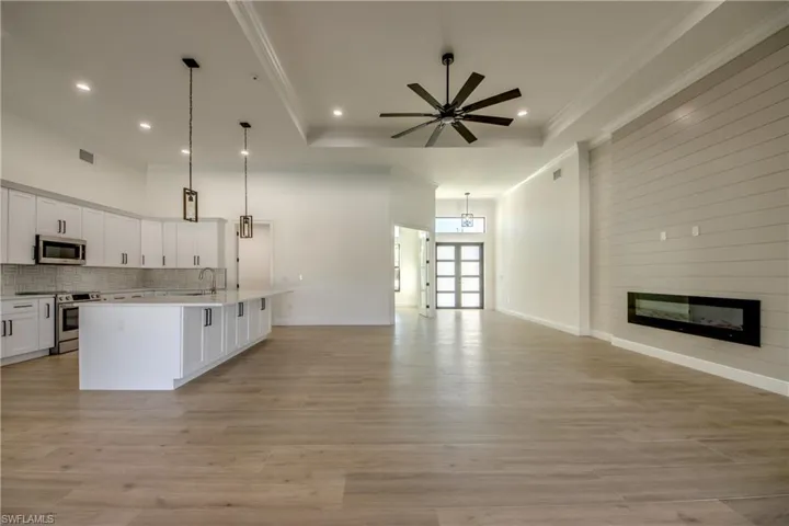 Kitchen featuring light hardwood / wood-style floors, a kitchen island with sink, a large fireplace, decorative light fixtures, and appliances with stainless steel finishes