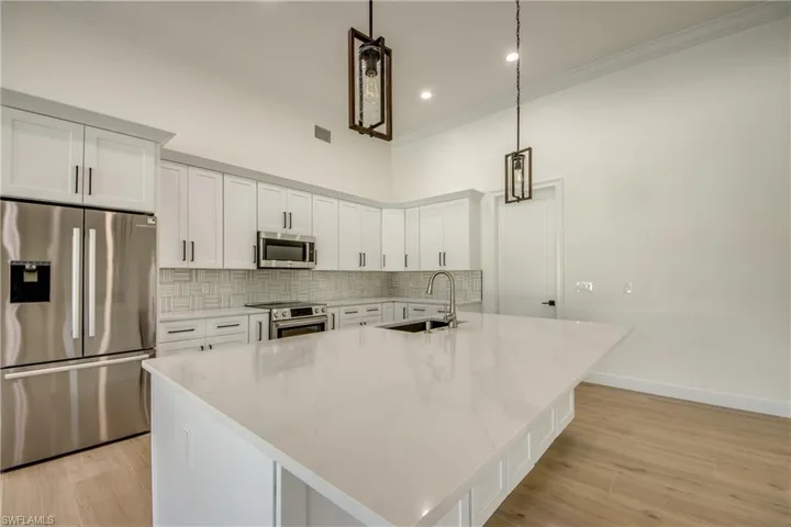 Kitchen featuring an island with sink, light wood-type flooring, stainless steel appliances, sink, and decorative light fixtures