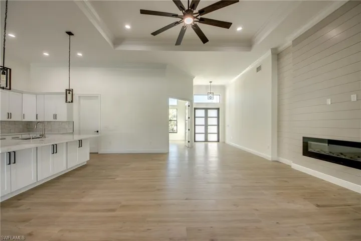 Unfurnished living room featuring light hardwood / wood-style floors, ceiling fan, crown molding, a raised ceiling, and sink