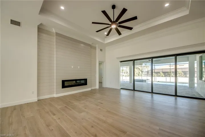 Unfurnished living room with ceiling fan, a tray ceiling, light hardwood / wood-style flooring, a fireplace, and ornamental molding