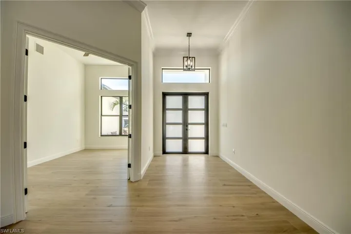 Entrance foyer featuring french doors, light wood-type flooring, crown molding, and a chandelier