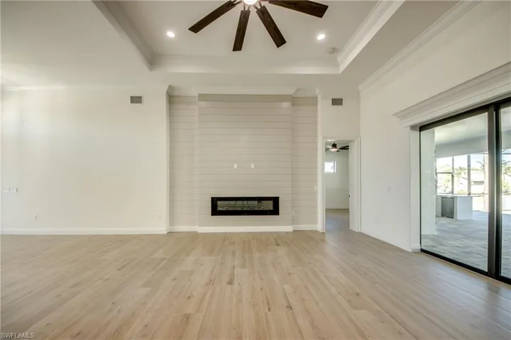 Unfurnished living room featuring a large fireplace, ornamental molding, a tray ceiling, and light hardwood / wood-style floors