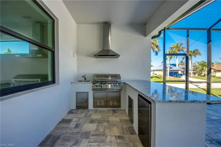 Kitchen with stainless steel fridge, sink, kitchen peninsula, exhaust hood, and light stone countertops