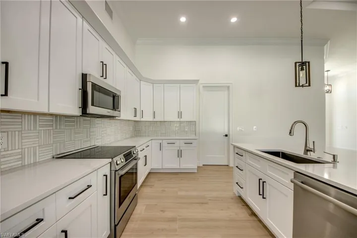 Kitchen with sink, light hardwood / wood-style floors, hanging light fixtures, white cabinetry, and appliances with stainless steel finishes