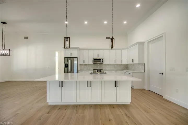 Kitchen with pendant lighting, appliances with stainless steel finishes, light wood-type flooring, and white cabinetry