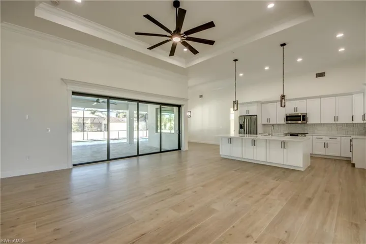 Kitchen with a kitchen island with sink, a raised ceiling, light hardwood / wood-style floors, pendant lighting, and appliances with stainless steel finishes
