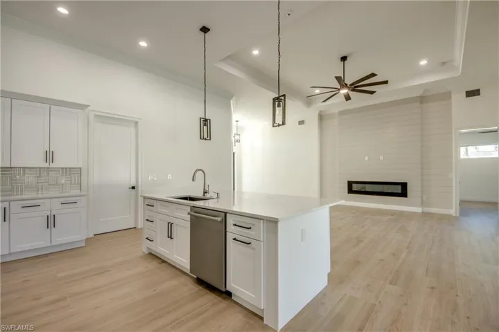 Kitchen featuring decorative light fixtures, sink, dishwasher, an island with sink, and white cabinets
