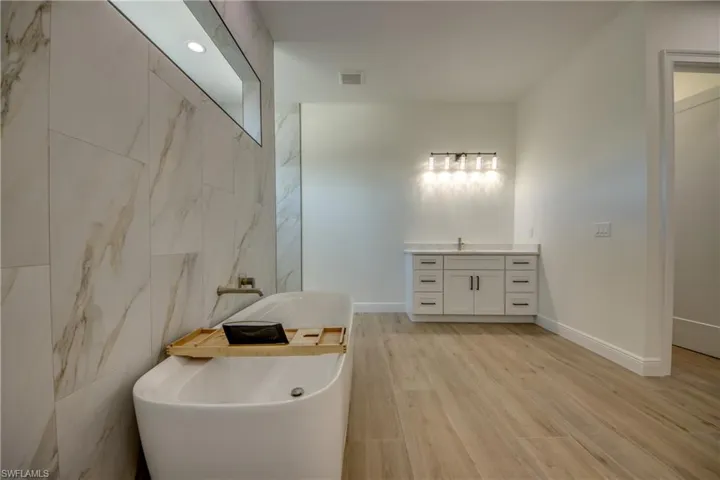 Bathroom featuring hardwood / wood-style flooring, a tub to relax in, tile walls, and vanity
