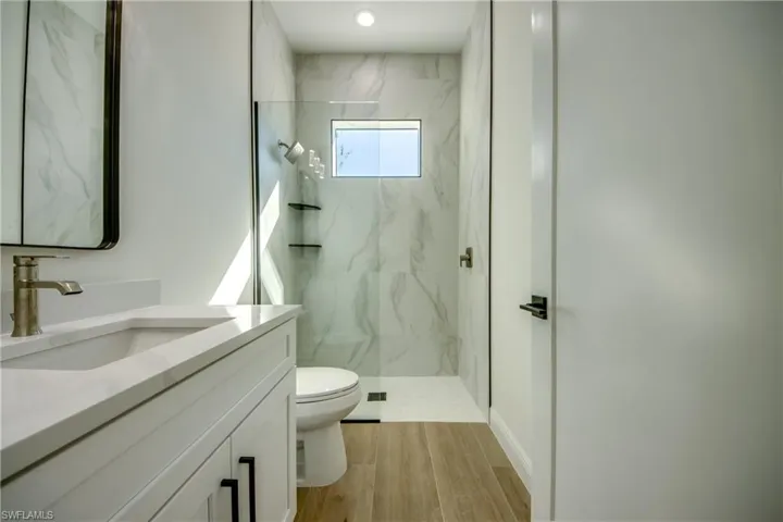 Bathroom with hardwood / wood-style flooring, vanity, tiled shower, and toilet