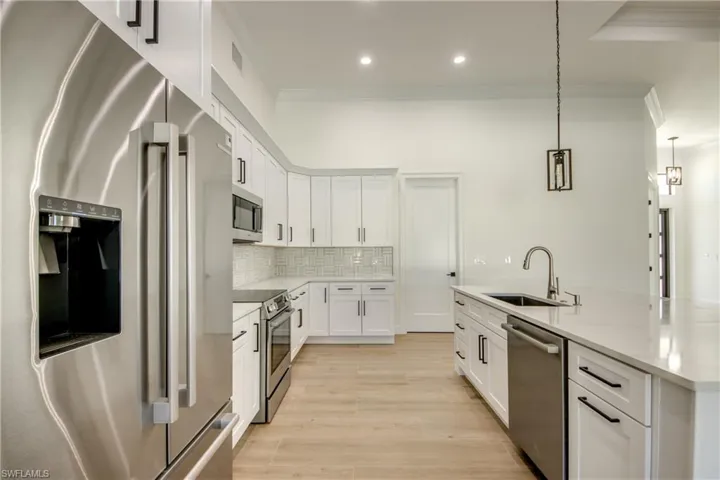 Kitchen with sink, decorative light fixtures, white cabinetry, stainless steel appliances, and light hardwood / wood-style floors
