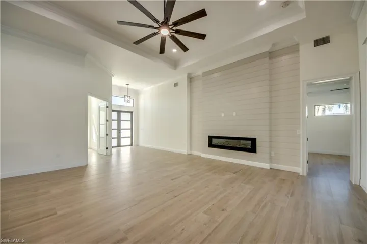 Unfurnished living room with ornamental molding, a tray ceiling, a large fireplace, and light hardwood / wood-style floors