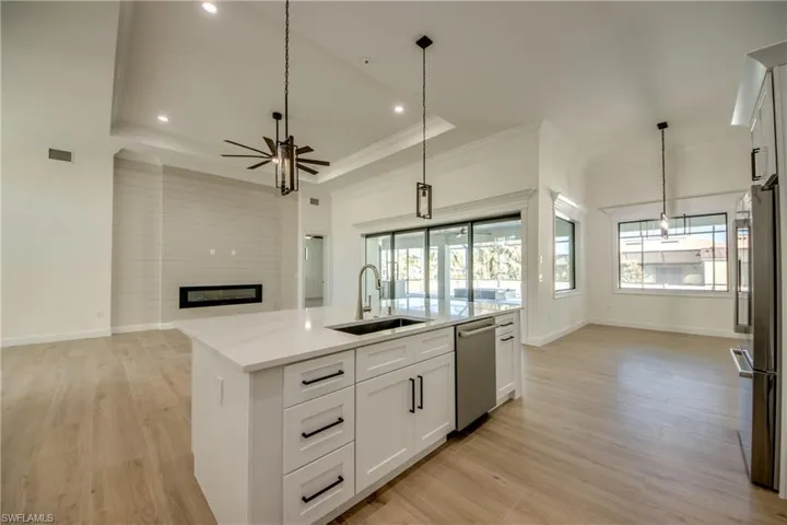 Kitchen featuring a center island with sink, sink, hanging light fixtures, appliances with stainless steel finishes, and white cabinetry