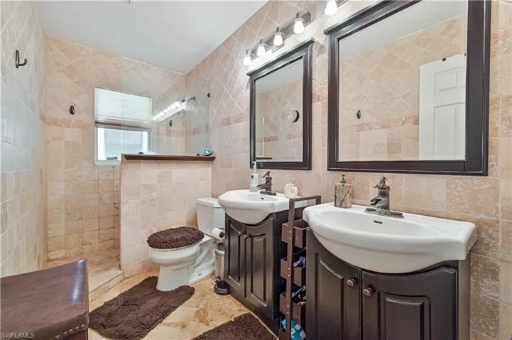 Bathroom featuring tile walls, two vanities, and a walk in shower