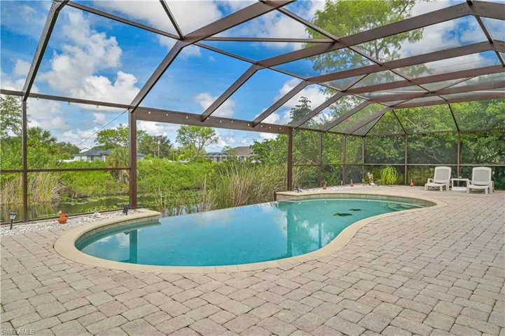 View of pool with a patio, an infinity pool, and glass enclosure