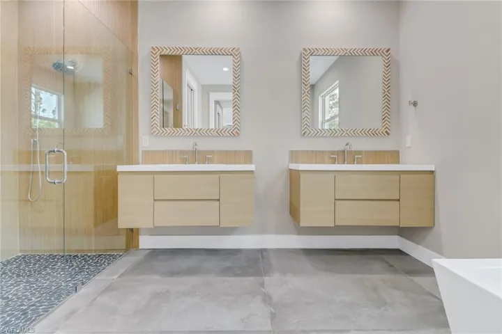 Full bathroom featuring a shower stall, two vanities, a freestanding bath, and concrete floors