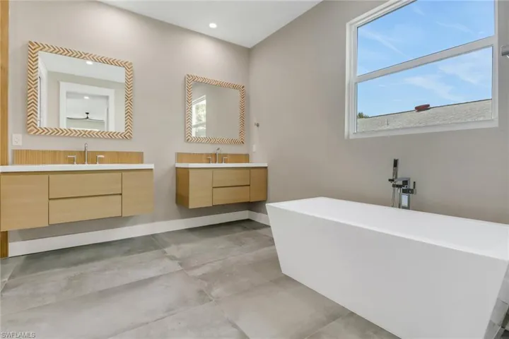 Bathroom with a freestanding bath, two vanities, concrete floors, and recessed lighting