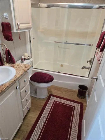 Full bathroom with wood-type flooring, vanity, shower / bath combination with glass door, and toilet