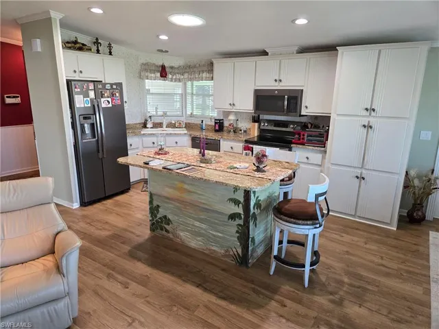 Kitchen featuring a breakfast bar, light hardwood / wood-style flooring, a kitchen island, stainless steel appliances, and white cabinets