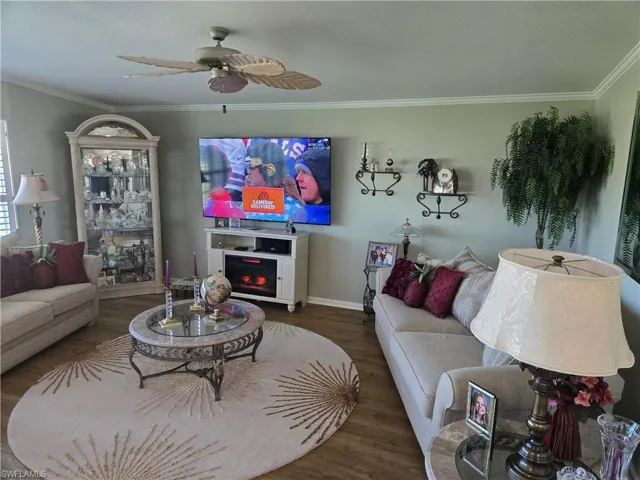 Living room featuring dark hardwood / wood-style flooring, ceiling fan, and crown molding
