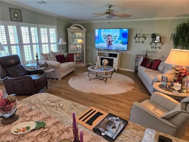 Living room featuring crown molding, vaulted ceiling, wood-type flooring, and ceiling fan