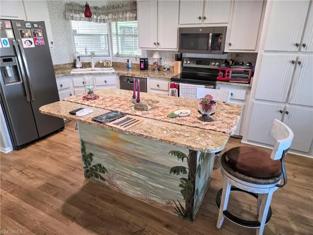 Kitchen featuring light stone counters, white cabinetry, a kitchen island, stainless steel appliances, and light hardwood / wood-style floors