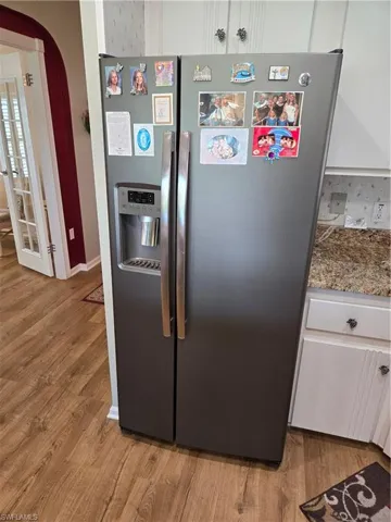 Kitchen with stainless steel refrigerator with ice dispenser, dark stone countertops, white cabinets, and light hardwood / wood-style floors
