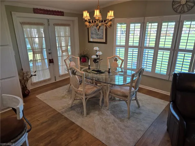 Dining room with dark wood-type flooring, ornamental molding, an inviting chandelier, and french doors