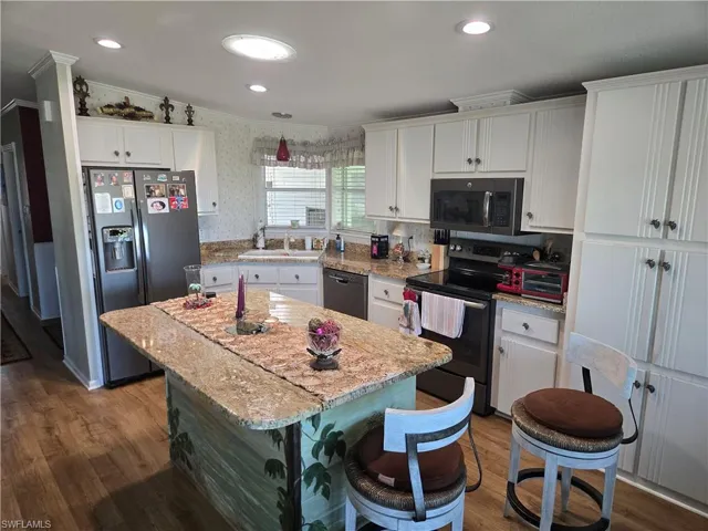Kitchen featuring a center island, ornamental molding, appliances with stainless steel finishes, light stone counters, and white cabinetry