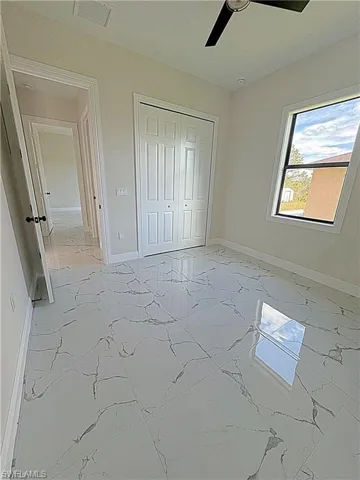 Unfurnished bedroom with light marble finish flooring, ceiling fan, and a closet