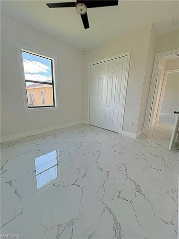 Unfurnished bedroom with light marble finish flooring, a closet, and a ceiling fan