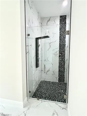 Full bath with light marble finish flooring and a marble finish shower