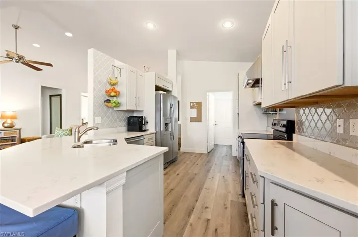 Kitchen featuring a peninsula, stainless steel appliances, Luxury Vinyl flooring, white cabinets, and recessed lighting